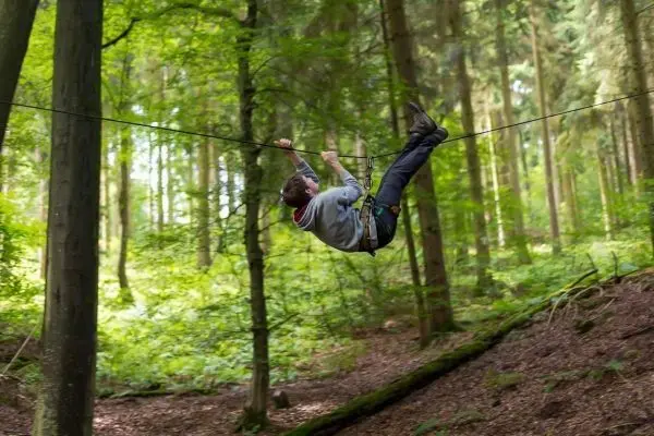 Person schwingt an einer Seilüberquerung durch den Wald beim Survival Training