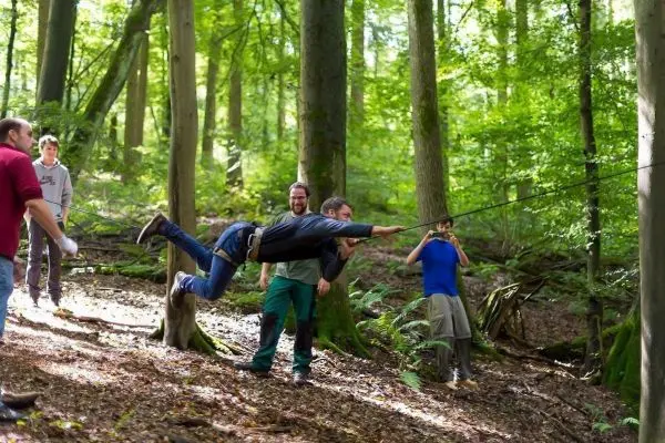 Person schwingt an Seil zwischen Bäumen im Wald beim Survival Training