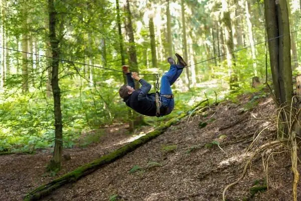 Person schwingt an selbstgebauter Seilbrücke durch den Wald