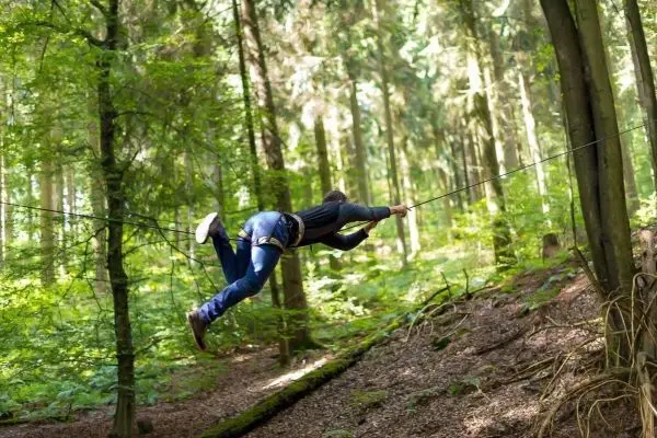 Person schwingt an selbstgebauter Seilbrücke durch den Wald