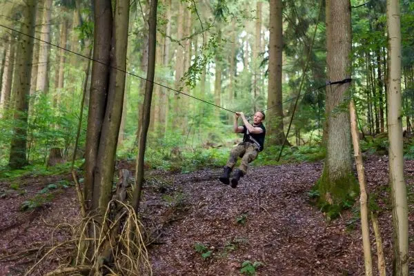 Person schwingt an selbstgebauter Seilbrücke durch den Wald