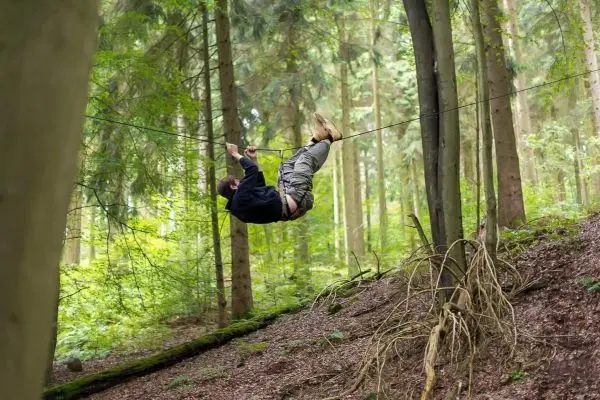 Person schwingt an selbstgebauter Seilbrücke zwischen Bäumen