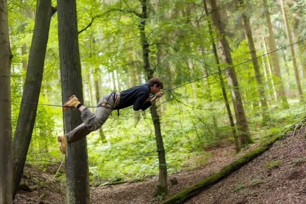 Person schwingt an selbstgebauter Seilbrücke zwischen Bäumen