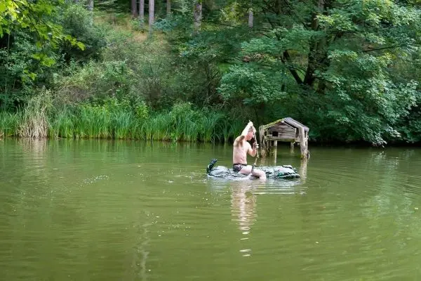 Person sitzt auf einem Floß im Wasser und hält einen Stock hoch