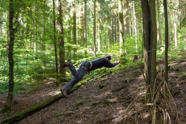 Person springt über eine selbstgebaute Seilbrücke im Wald