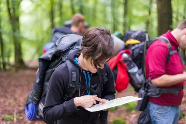 Person studiert Karte im Wald, Rucksäcke im Hintergrund
