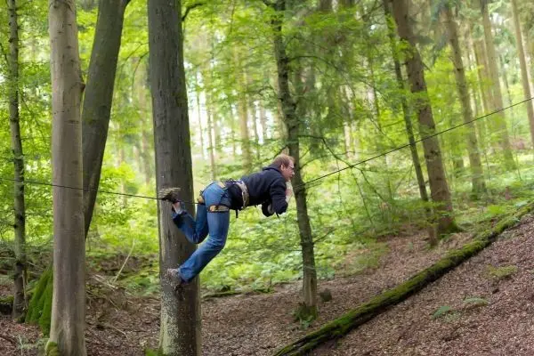 Person überquert eine selbstgebaute Seilbrücke zwischen zwei Bäumen