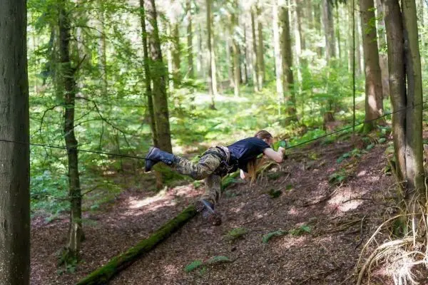 Person überquert selbstgebaute Seilbrücke im Wald beim Survival Training