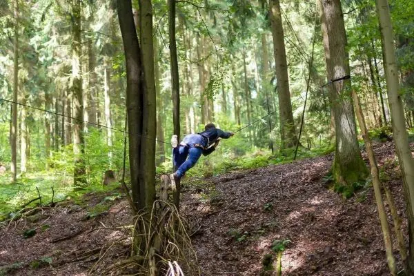 Person überquert selbstgebaute Seilbrücke zwischen Bäumen