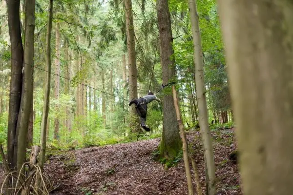Person überquert selbstgebaute Seilbrücke zwischen Bäumen im Wald