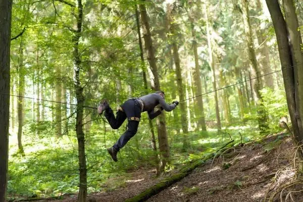 Person überquert selbstgebaute Seilbrücke zwischen Bäumen im Wald
