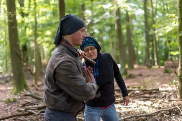Person zeigt einer anderen Person eine Technik im Wald