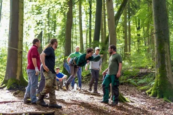 Seilquerung mit mehreren Personen im Wald, eine Person überquert an einem Seil