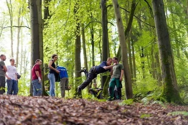 Teilnehmer überquert eine selbstgebaute Seilbrücke im Wald