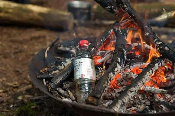 Wasserflasche steht zwischen brennenden Ästen im Feuer