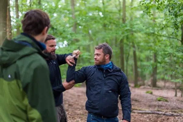 Zwei Personen demonstrieren eine Technik im Wald, während eine dritte Person zuschaut