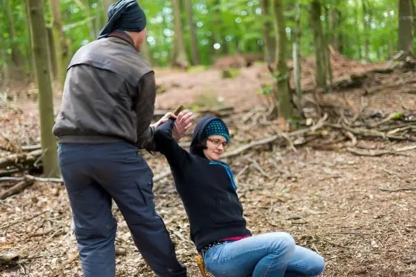 Zwei Personen im Wald, eine zieht die andere am Handgelenk nach hinten