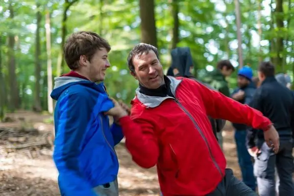 Zwei Personen in Jacken interagieren spielerisch im Wald