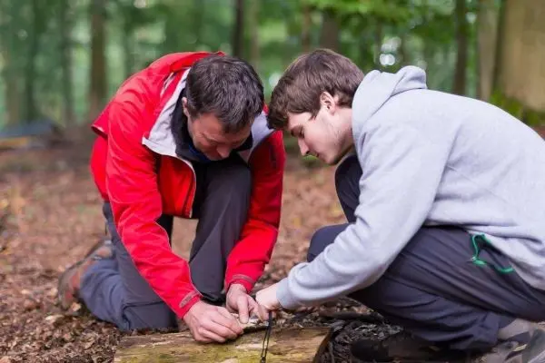 Zwei Personen knien auf dem Boden und binden Seile an einem Holzstück