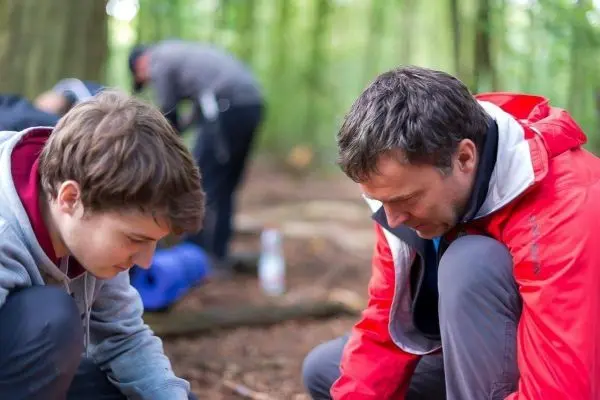 Zwei Personen knien im Wald und konzentrieren sich auf eine Tätigkeit am Boden