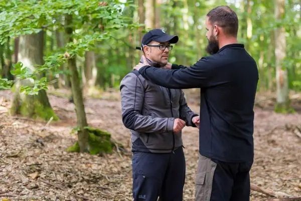 Zwei Personen stehen im Wald und üben eine Technik zur Selbstverteidigung