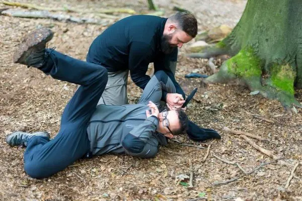 Zwei Personen üben Bodenkampftechniken auf dem Waldboden