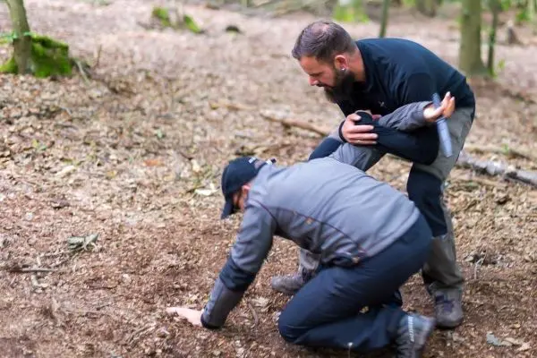 Zwei Personen üben eine Erste-Hilfe-Maßnahme auf dem Waldboden aus