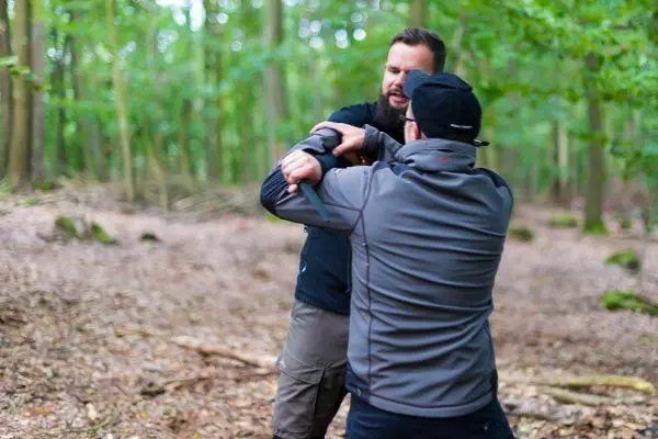 Zwei Personen üben eine Nahkampftechnik im Wald