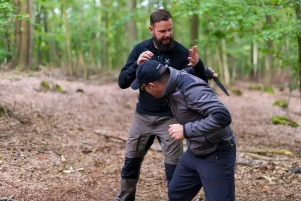 Zwei Personen üben eine Selbstverteidigungstechnik im Wald mit einem Messer