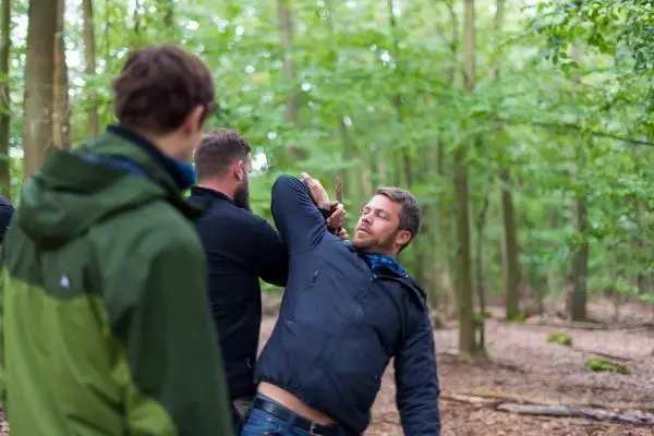Zwei Personen üben eine Selbstverteidigungstechnik im Wald mit einem Stock