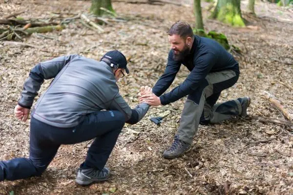 Zwei Personen üben eine Technik im Wald, eine Person greift nach der anderen