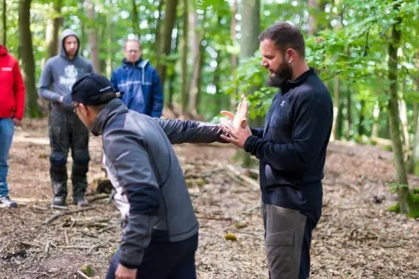 Zwei Personen üben eine Technik im Wald, während andere zuschauen