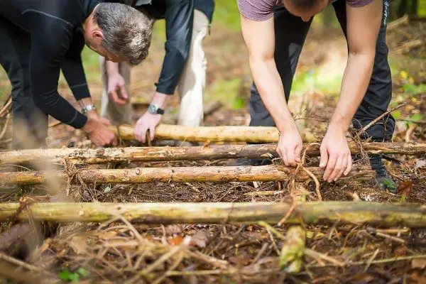 Drei Personen bauen eine Holzstruktur aus Ästen im Wald