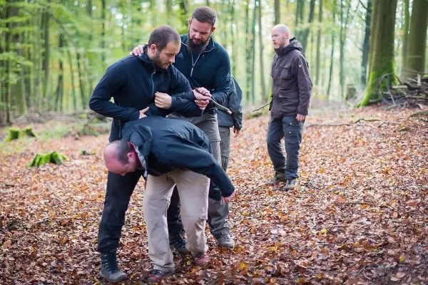 Drei Personen üben eine Technik im Wald, eine Person wird gehalten