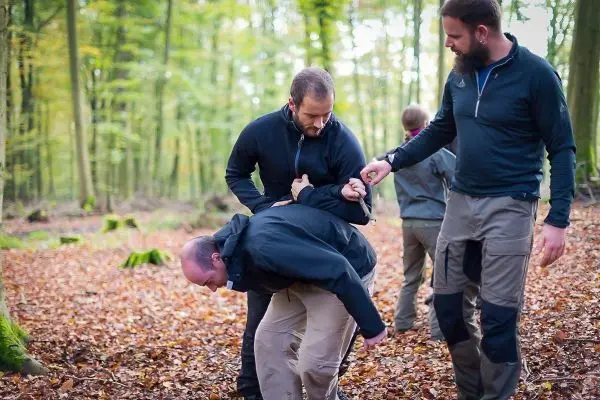 Drei Personen üben eine Technik zur Kontrolle eines Gegners im Wald