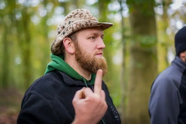 Ein Mann mit einem Hut zeigt mit dem Finger in den Wald