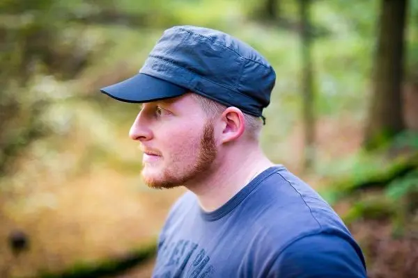 Ein Mann mit einer Kappe steht im Wald und schaut nachdenklich zur Seite