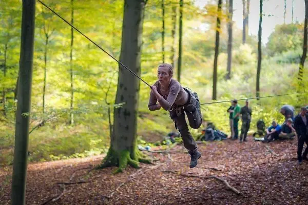 Frau überquert selbstgebaute Seilbrücke zwischen Bäumen im Wald