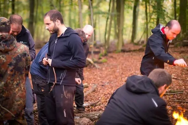 Gruppe arbeitet am Bodenfeuer im Wald, Holz und Zunder sind sichtbar