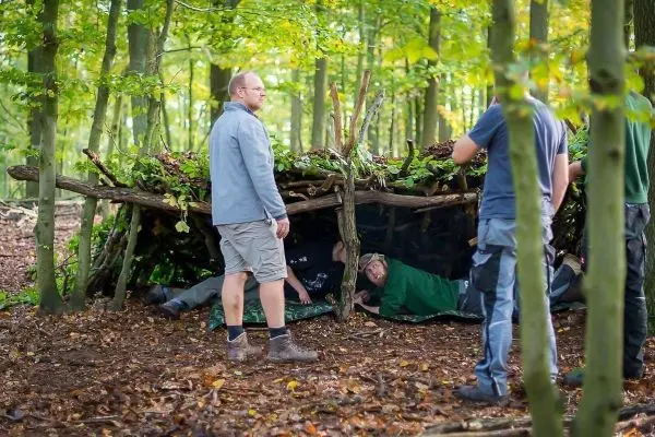 Gruppe baut Tarp-Notunterkunft aus Ästen und Blättern im Wald