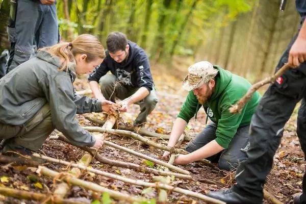 Gruppierung arbeitet am Boden mit Ästen zur Konstruktion einer improvisierten Struktur