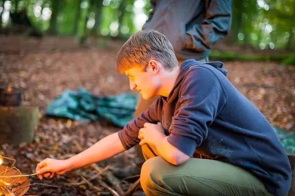 Junge hält Stock über kleines Bodenfeuer im Wald