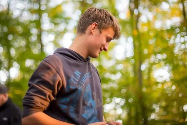 Junge mit Kapuzenpullover steht in einem Wald und schaut nach unten