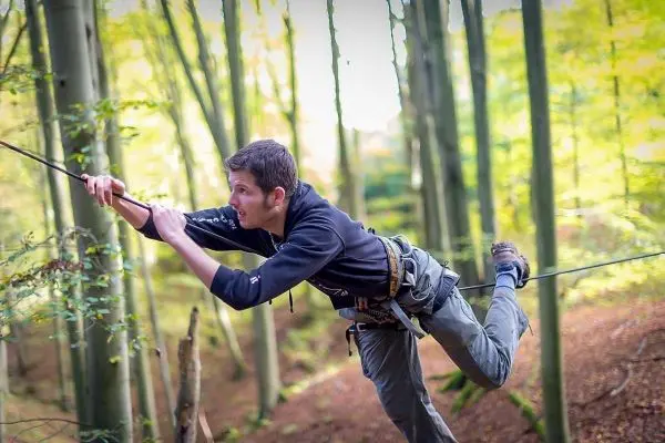 Junge überquert selbstgebaute Seilbrücke zwischen Bäumen im Wald