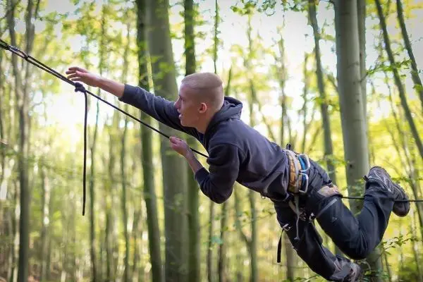 Junge überquert selbstgebaute Seilbrücke zwischen Bäumen im Wald