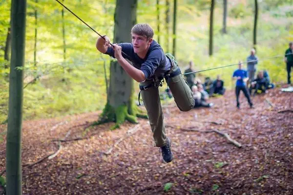 Junge überquert selbstgebaute Seilbrücke zwischen Bäumen im Wald