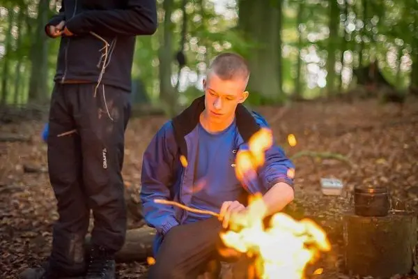 Kleine Flamme brennt im Wald, eine Person sitzt davor und beobachtet sie