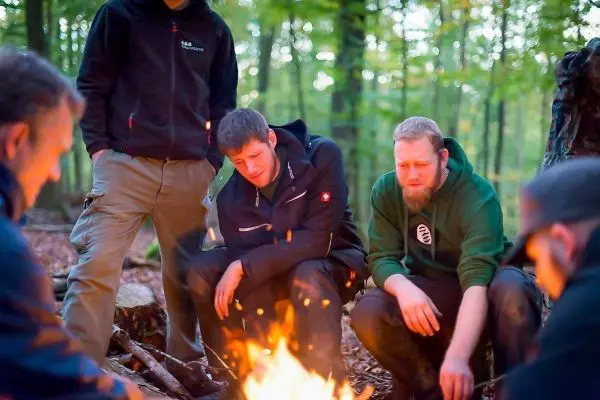 Kleines Bodenfeuer in einem Wald, mehrere Personen sitzen darum herum