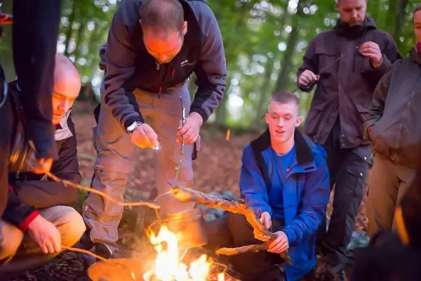 Männer um ein kleines Feuer, einer hält einen Stock über die Flamme