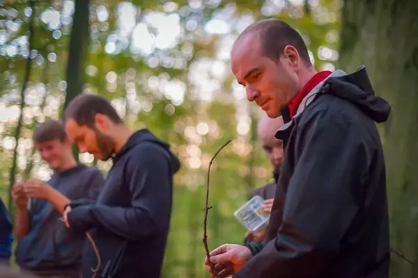 Mann hält einen Stock in der Hand, während andere Personen im Hintergrund beschäftigt sind